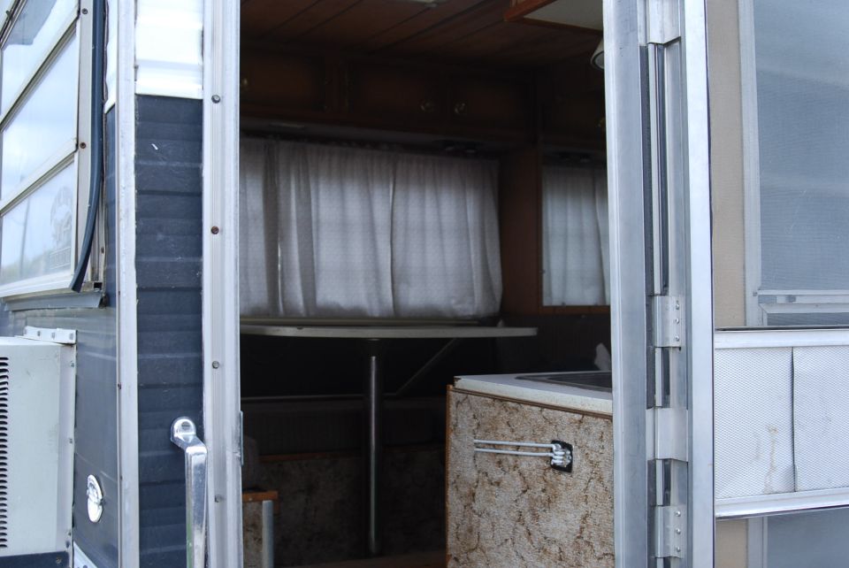 Interior view of a camper, showing curtains, a table, and cabinetry