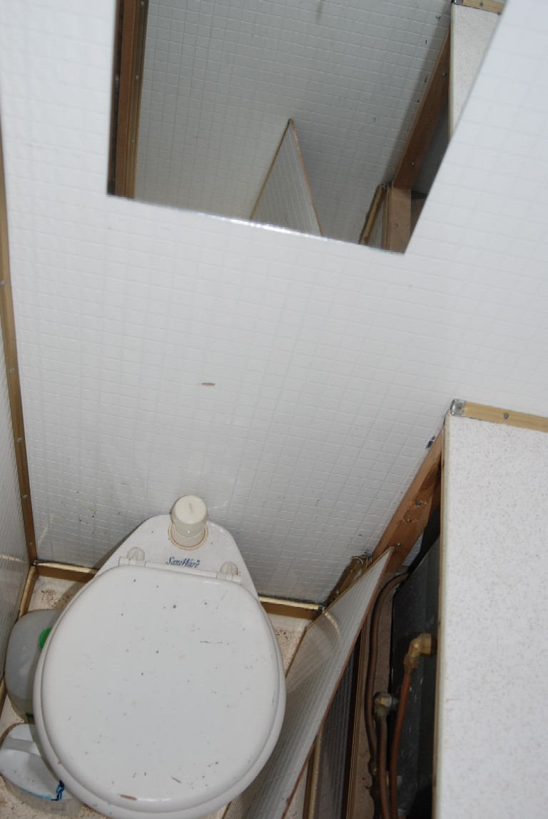 Camper interior showing a white toilet with a beige lid and a white tank