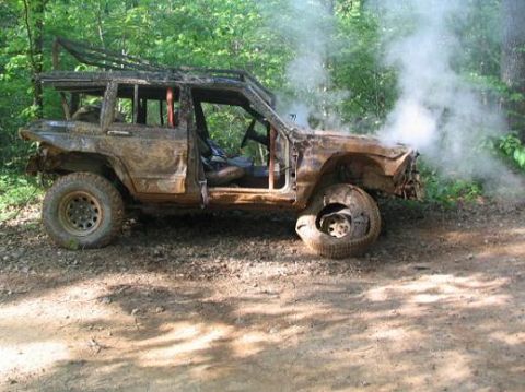 1990 Ford Bronco - This heavily damaged off-road vehicle is emitting smoke, suggesting it has recently been in an accident or experienced mechanical failure.