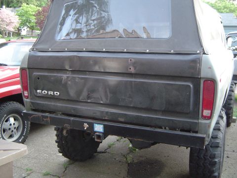 1978 Ford Bronco - Rear view of a 1978 Ford Bronco with a dented tailgate and a soft top, parked next to a red vehicle.