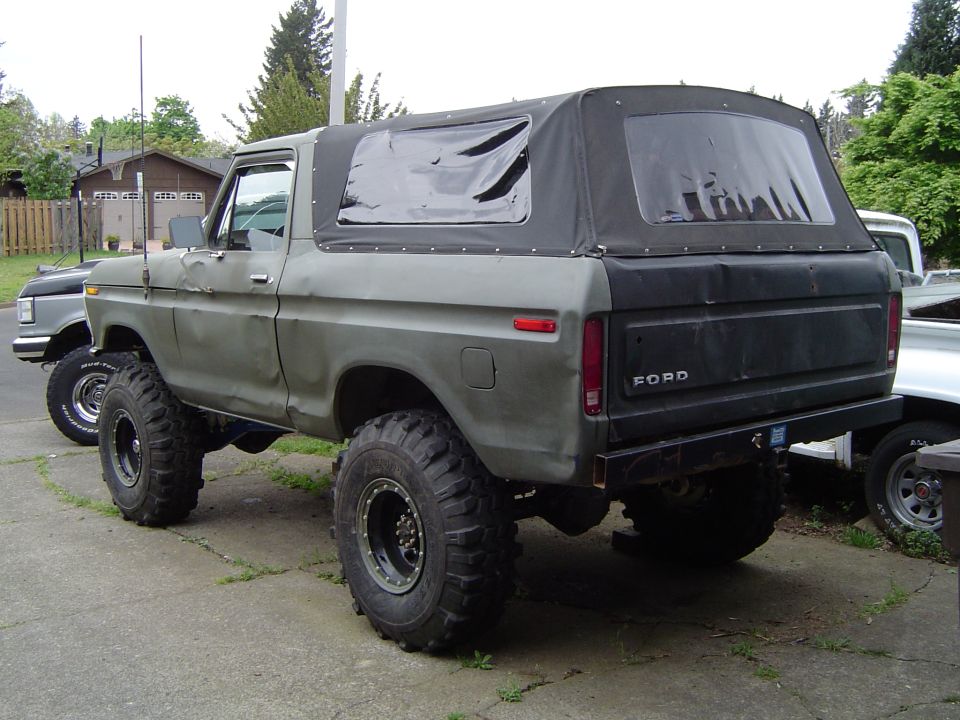 1978 Ford Bronco with soft top, lifted with large tires, parked on driveway. Another truck is visible to the left