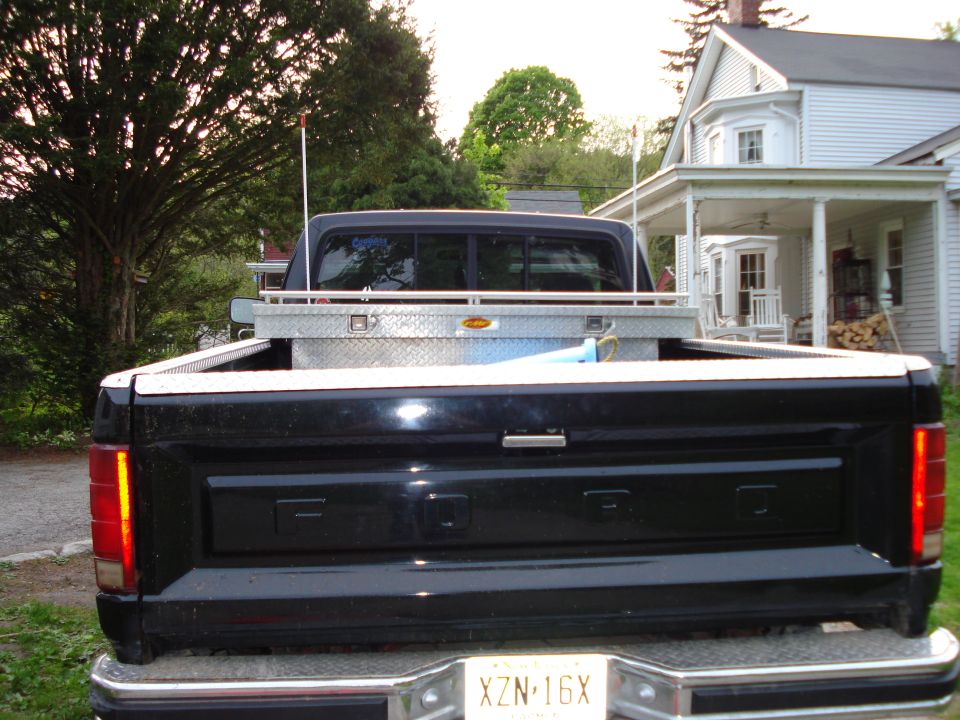 Black Ford pickup truck rear view, with a toolbox in the bed and a house in the background