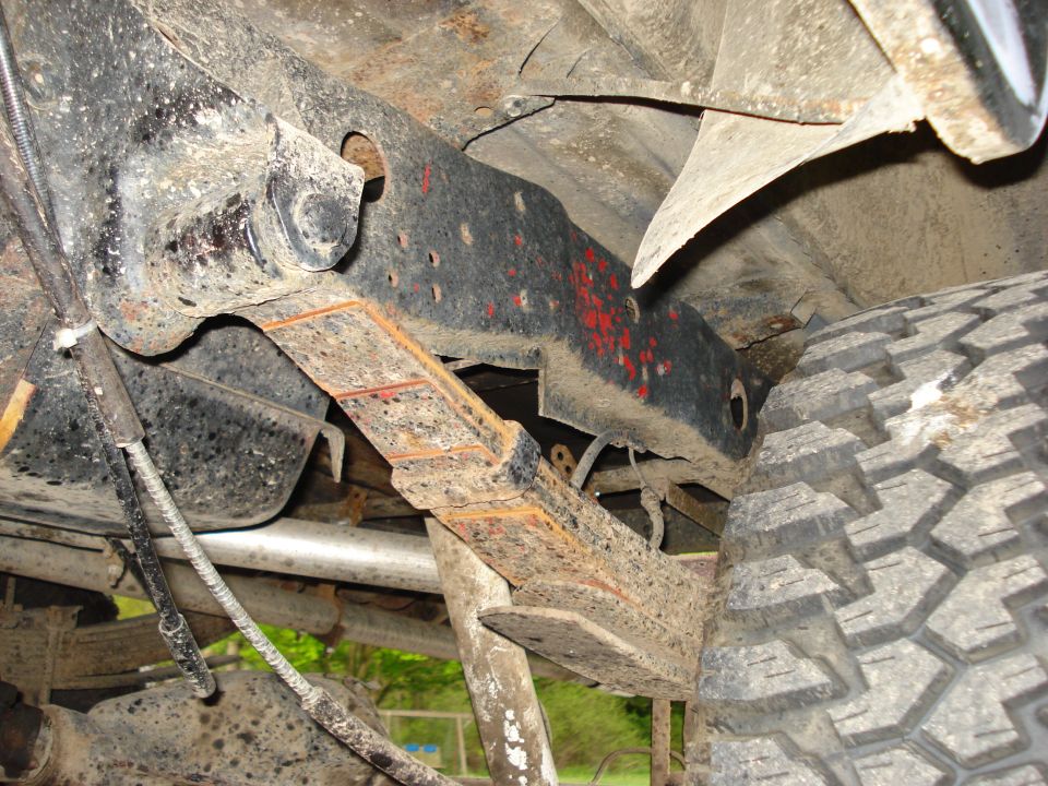 Close-up of rusty leaf springs and frame of a truck. Tire visible on the right