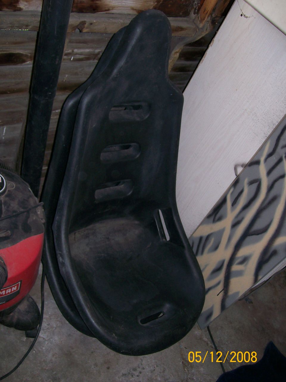 two black plastic bucket seats stacked, leaning against a wall with a shop vac nearby