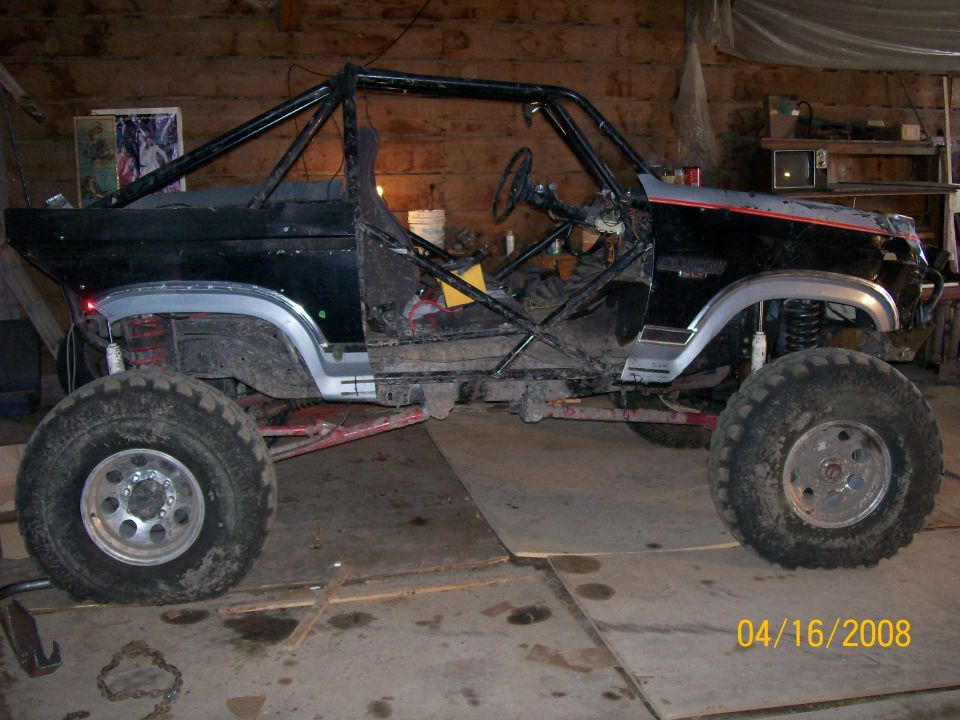 Black and silver Ford SUV stripped to its roll cage on a lift kit in a garage