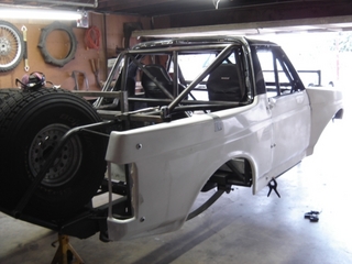 1996 Ford Bronco - A white Ford Bronco body is being worked on in a garage, showing its custom roll cage and spare tire.