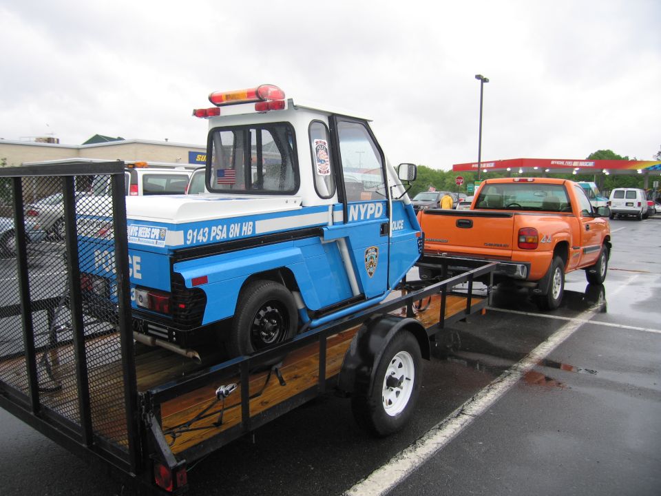 NYPD blue three-wheeled scooter on a flatbed trailer behind orange truck
