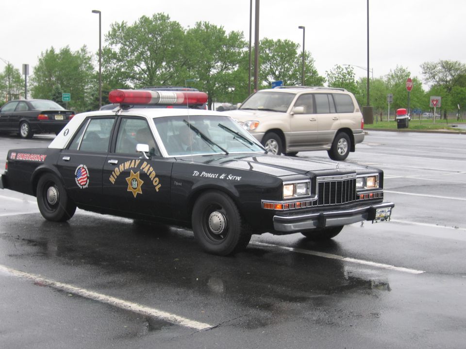 Black-and-white Highway Patrol sedan with roof light bar, front quarter