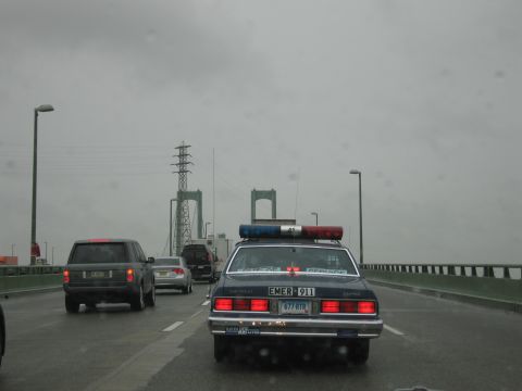 1991 Ford LTD Crown Victoria - Rear view of a dark Chevrolet Caprice EMER 911 cruiser with light bar crossing a bridge roadway in the rain.