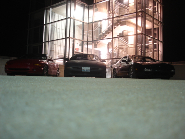 Three cars parked in front of a glass building at night. The middle car has license plate 'N60 3832'