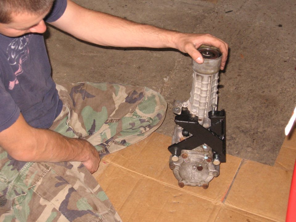 Man steadying an aluminum rear differential with black X mount bracket on garage floor