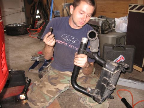 1991 Mitsubishi 3000GT - Mechanic works on a radiator and hoses in a garage setting.