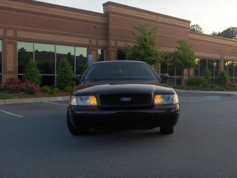 2001 Ford Crown Victoria - A black 2001 Ford Crown Victoria is parked in front of a modern office building with large windows.