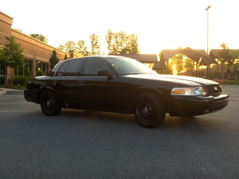 2001 Ford Crown Victoria - A black 2001 Ford Crown Victoria is parked outside a building during sunset.