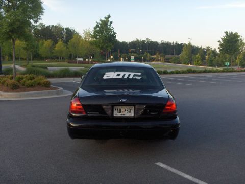 2001 Ford Crown Victoria - Rear view of a black 2001 Ford Crown Victoria parked in a lot, showing the license plate and a window sticker.