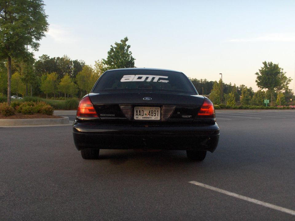 Black Ford Crown Victoria parked in a lot, rear view. Has a 'BOTT' sticker on the back window and license plate AAD-4891