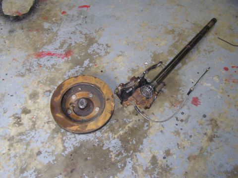 1993 Ford Bronco - A rusty brake rotor and a disassembled axle assembly with a brake cable are shown lying on a concrete floor. The parts appear to be from a…