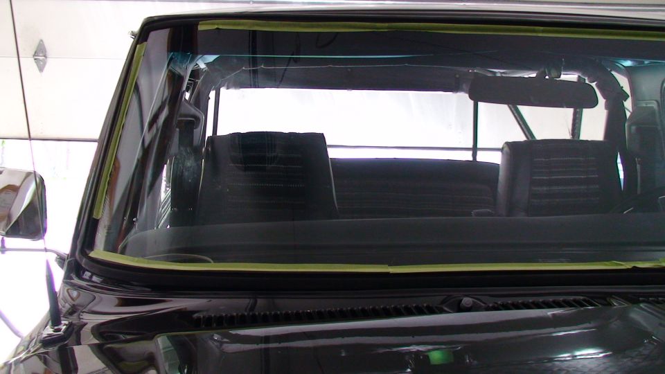 Front view of a black vehicle's windshield with masking tape, showing interior seats and rearview mirror.