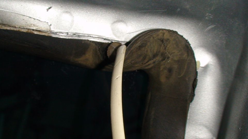 Close-up of a cream tool prying a dark rubber seal from a silver vehicle body.