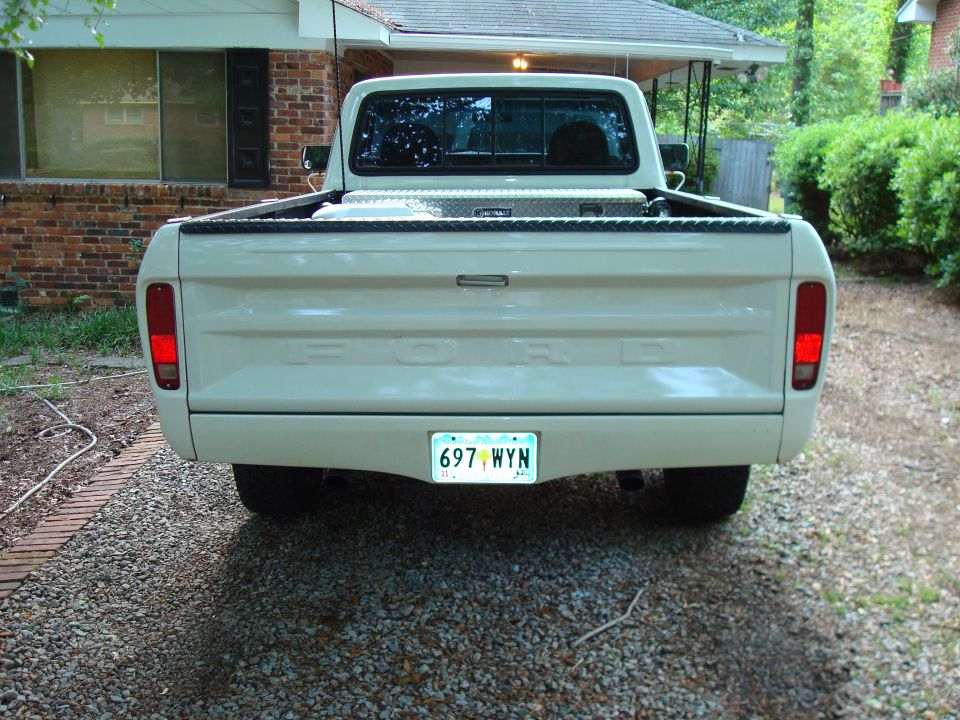 Rear view of a light-colored 1977 Ford F-100 pickup truck with a toolbox and license plate.