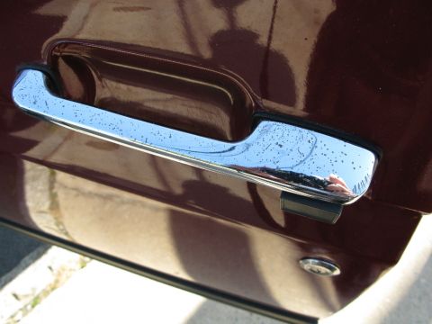 1991 Ford F-150 - A close-up view of a chrome door handle on a dark red vehicle. The handle shows some pitting and water spots, reflecting the surrounding en…
