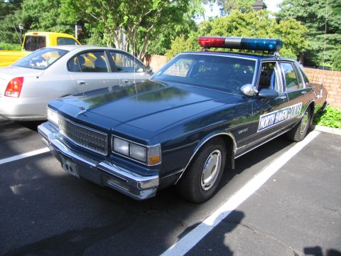 1991 Ford LTD Crown Victoria - dark blue North Haven Police Chevrolet Caprice sedan with light bar parked beside a silver car under trees.
