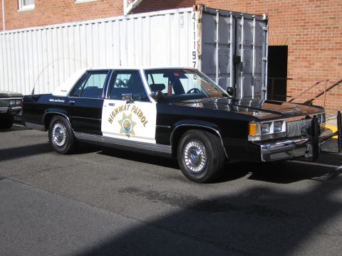 1991 Ford LTD Crown Victoria - black-and-white Highway Patrol Ford LTD Crown Victoria sedan with star emblem parked beside a shipping container.