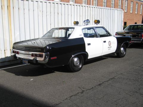 1991 Ford LTD Crown Victoria - Rear view of a black-and-white LAPD police sedan with twin roof lights parked by a white fence, another cruiser at right.
