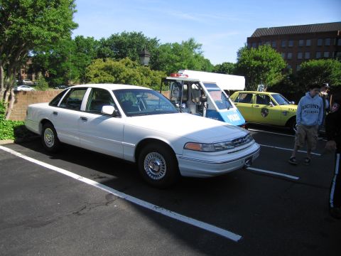 1991 Ford LTD Crown Victoria - white Ford Crown Victoria sedan parked at an outdoor car gathering next to a small NYPD vehicle and a yellow taxi-style car.