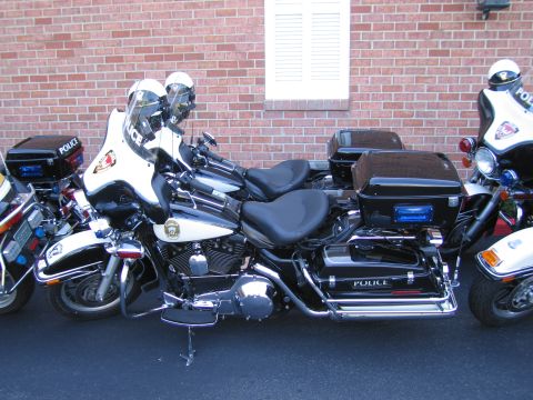 1991 Ford LTD Crown Victoria - black-and-white Police Harley-Davidson motorcycle with hard saddlebags parked in front of a brick wall.