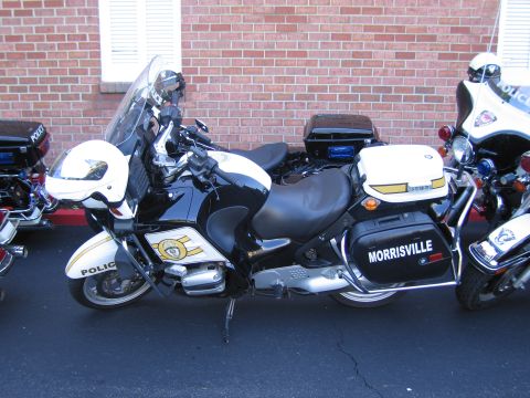 1991 Ford LTD Crown Victoria - white BMW Police motorcycle lettered Morrisville parked against a brick wall among other police bikes.