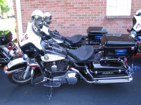 1991 Ford LTD Crown Victoria - black-and-white Police Harley-Davidson motorcycle with chrome exhaust and hard cases, parked beside a brick wall.