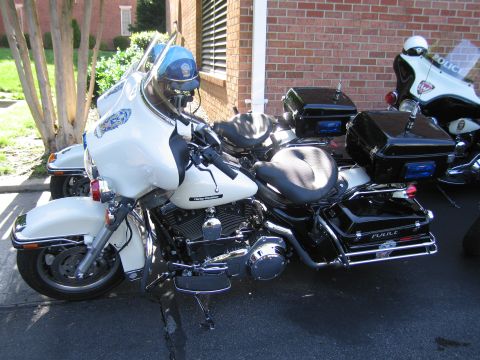 1991 Ford LTD Crown Victoria - white Police Harley-Davidson motorcycle with a windshield and rear top case parked on a driveway by a brick building.