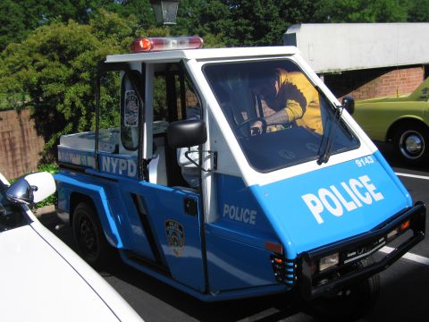 1991 Ford LTD Crown Victoria - blue-and-white NYPD three-wheeled enclosed police scooter with a roof lightbar and a person seated inside.