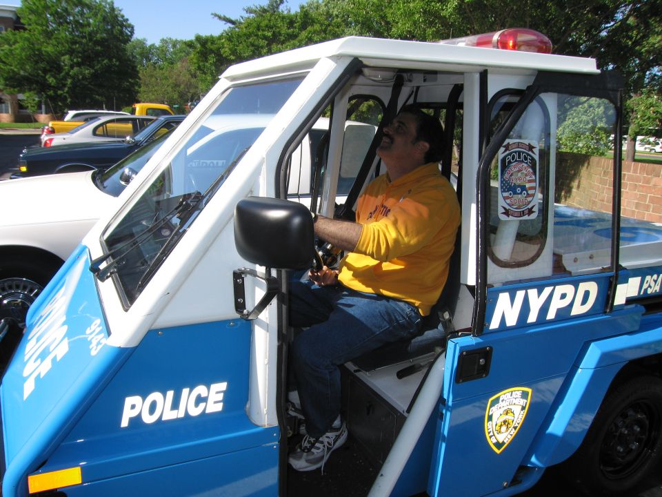 Man in yellow shirt seated in a blue NYPD three-wheeled police scooter