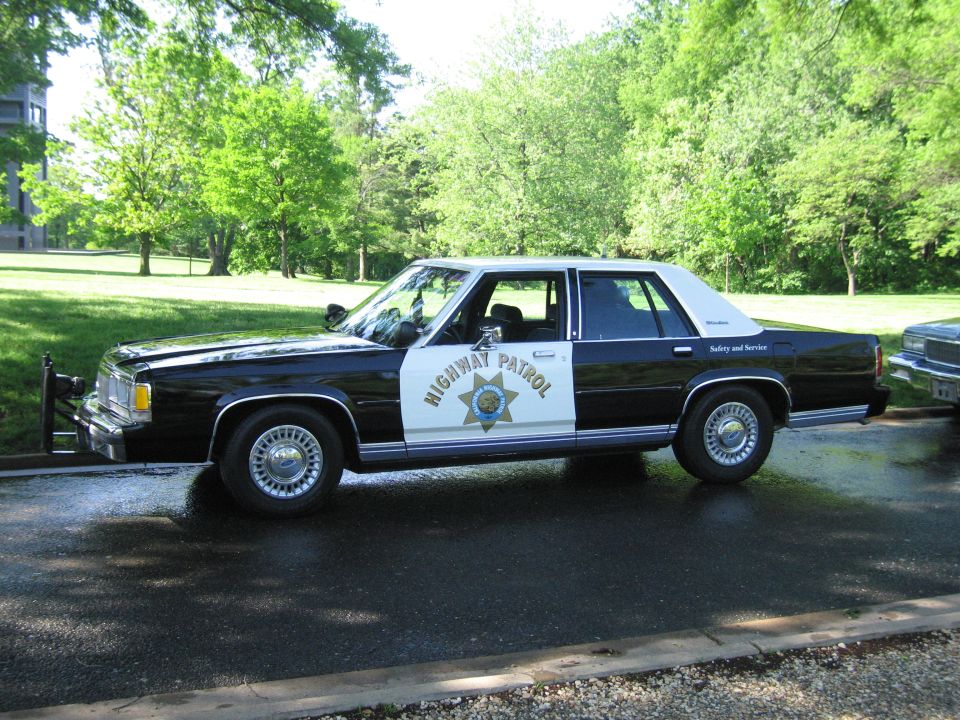 Black and white Highway Patrol sedan in profile beside another car in a park