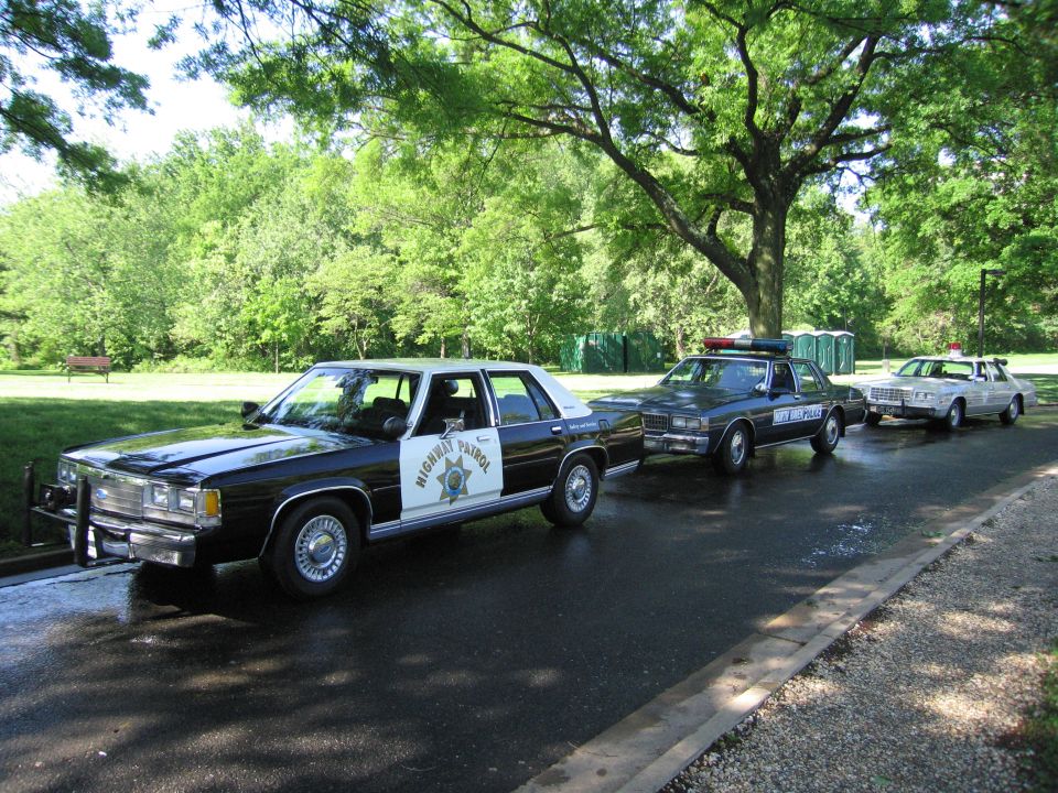 Row of three vintage police cars parked on a wet road in a green park