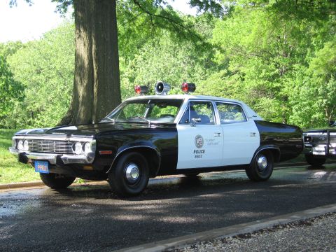 1991 Ford LTD Crown Victoria - Front three-quarter view of a vintage black-and-white Police sedan with twin roof spotlights and red beacons, parked in a park.