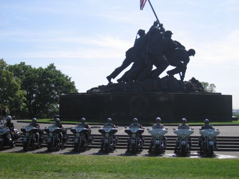1991 Ford LTD Crown Victoria - row of police motorcycles parked before the bronze Iwo Jima flag-raising memorial statue under a clear blue sky.