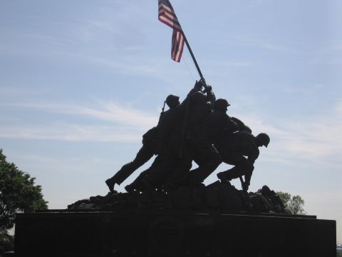 1991 Ford LTD Crown Victoria - Backlit silhouette of the Iwo Jima flag-raising memorial statue with figures hoisting a U.S. flag against a pale blue sky.