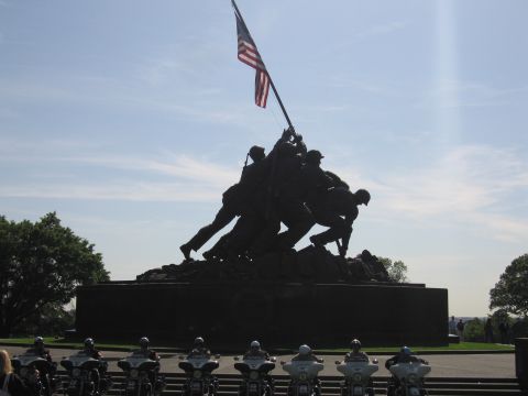 1991 Ford LTD Crown Victoria - bronze Iwo Jima flag-raising memorial statue with U.S. flag, fronted by a row of motorcycles under a blue sky.