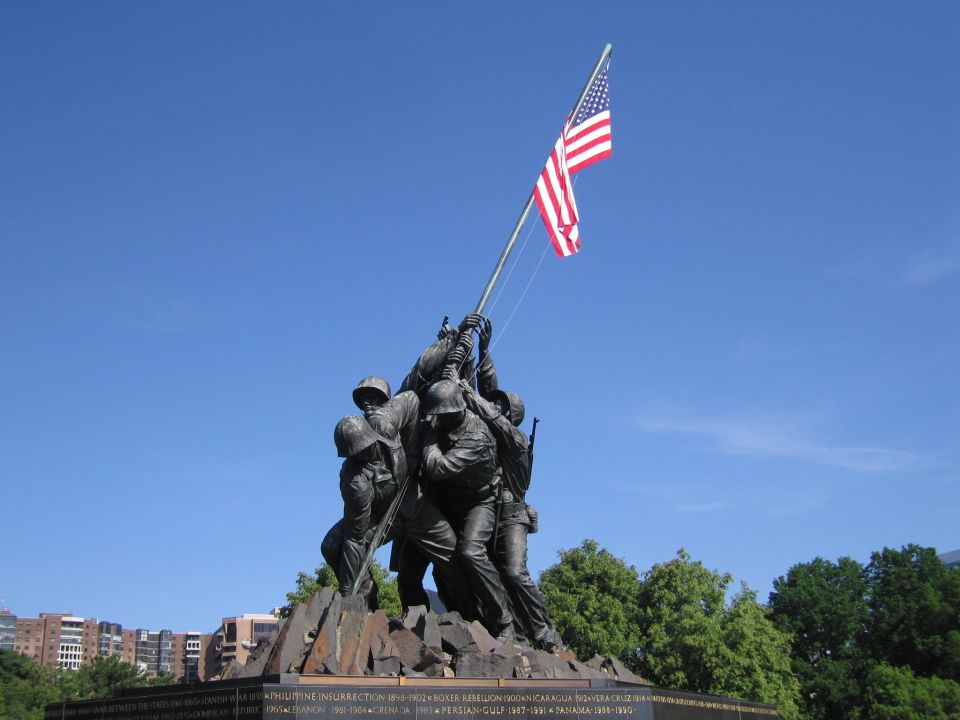Bronze Marine Corps War Memorial statue raising US flag against blue sky