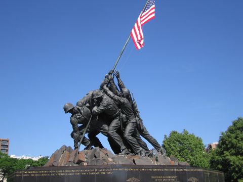 1991 Ford LTD Crown Victoria - Marine Corps War Memorial flag-raising statue rises above an inscribed granite base listing campaigns, under a blue sky.