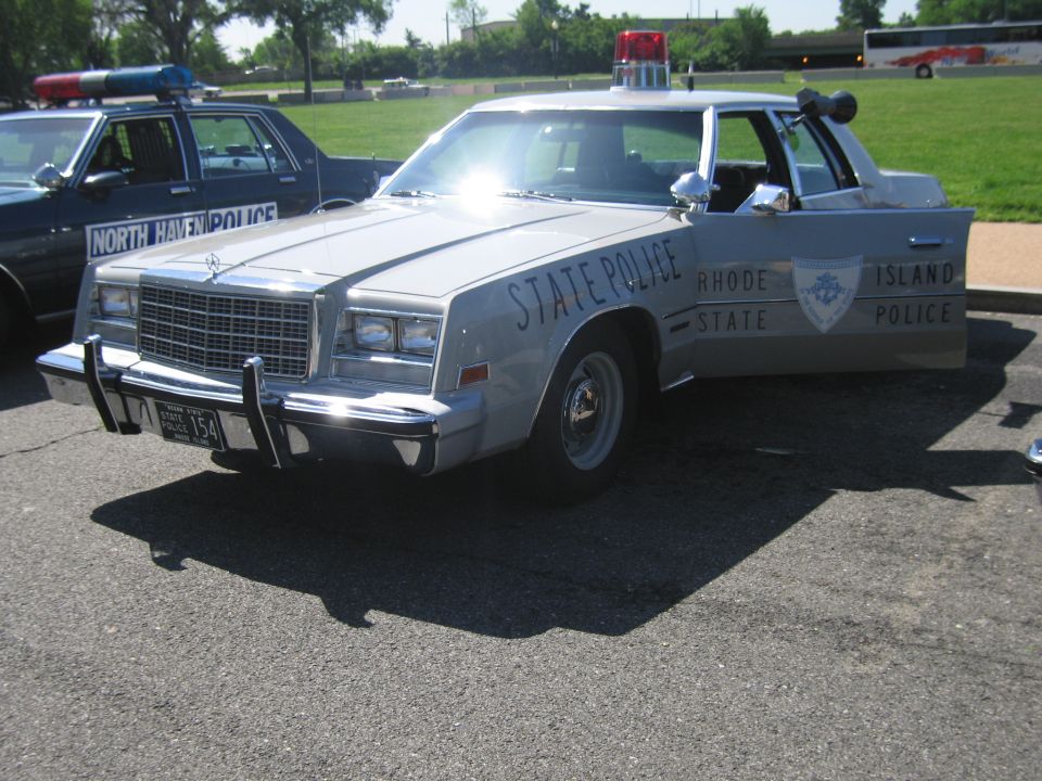 Silver Rhode Island State Police sedan with sun glare and roof beacon