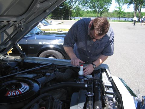 1991 Ford LTD Crown Victoria - man in a blue shirt and sunglasses leans over the open engine bay of a black police car, working on the engine.