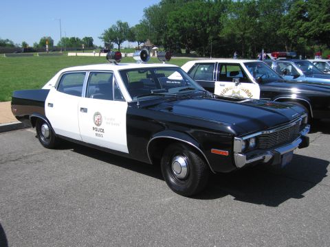 1991 Ford LTD Crown Victoria - black-and-white Police sedan with twin roof speakers and a city shield door emblem parked among other patrol cars.