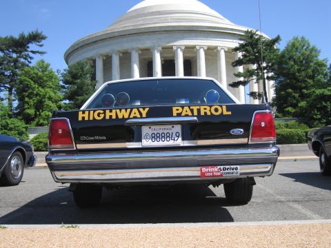 1991 Ford LTD Crown Victoria - rear of a black Ford Crown Victoria Highway Patrol car with California plate, parked before a white domed memorial.