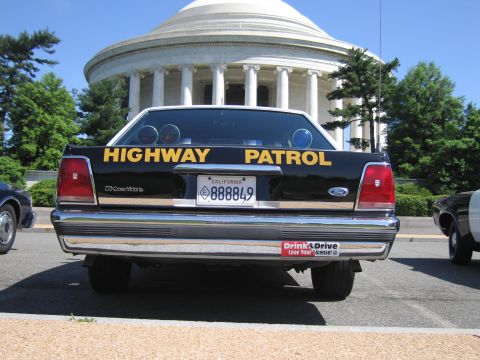 1991 Ford LTD Crown Victoria - rear of a black Ford Crown Victoria Highway Patrol car with twin roof spotlights and California plate before a domed memorial.