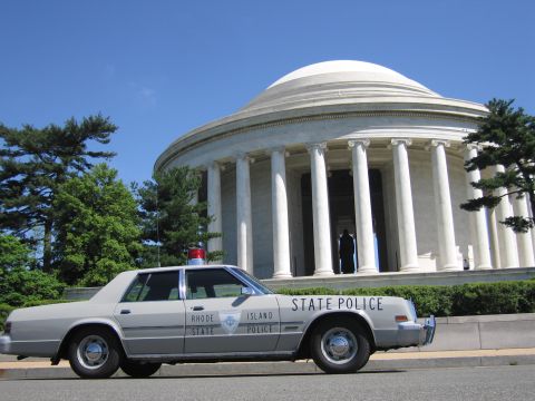 1991 Ford LTD Crown Victoria - gray State Police sedan with a red roof light is parked on pavement before the white domed Jefferson Memorial.