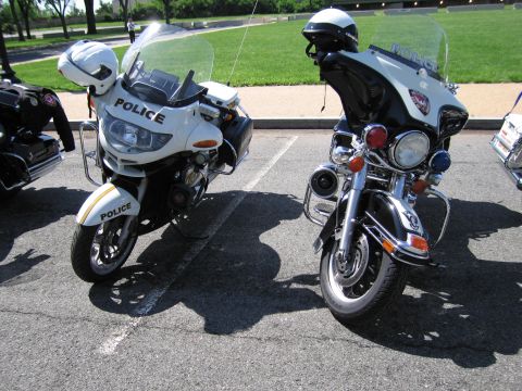 1991 Ford LTD Crown Victoria - white police motorcycle and a black police motorcycle, each marked Police with helmets, parked side by side on pavement.